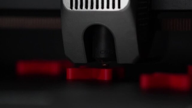 Close up of a 3D printer extruder printing red X shapes during the additive manufacturing process, detailed view of modern 3D printing technology in motion.