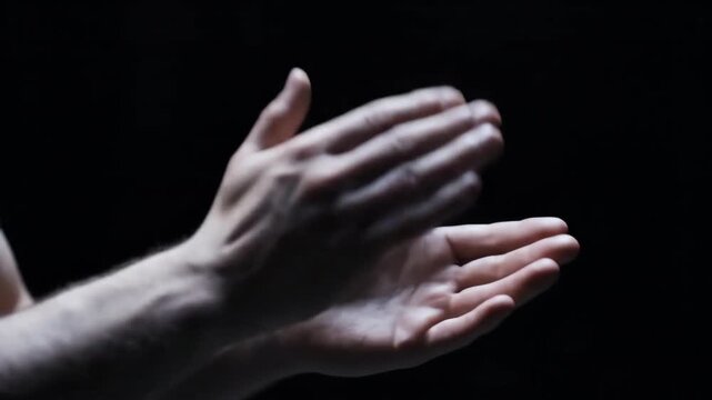 Person clapping hands together against a dark background close up