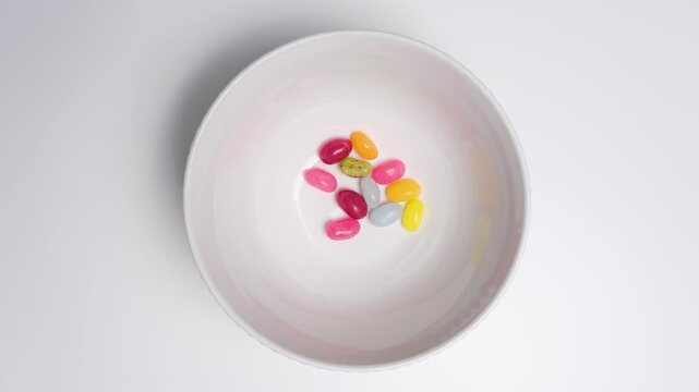Colorful jelly beans gradually disappear from a white bowl until empty, minimal top view, stop motion, sweet snack concept. Stop motion food background