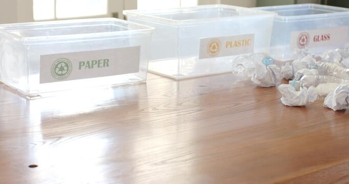 Sunlight is shifting, casting reflections on three recycling tubs and paper balls to aid sorting