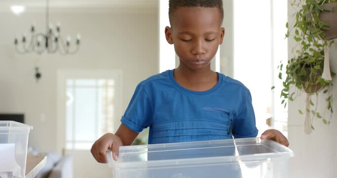 Reaching from right, African American boy child lifting PLASTIC bin, checking items in dining room