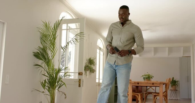 African American man walking through front door into entryway, using smartphone, checking outside