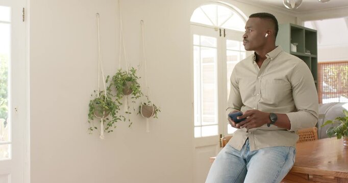 African American mid adult man holding smartphone on wooden counter, noticing entryway movement