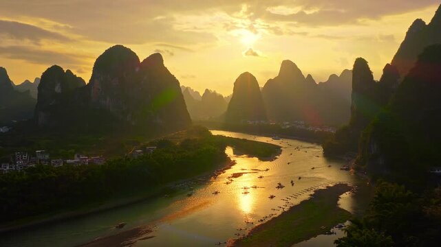 Sunset over majestic karst mountains and Li River in Guilin, China. Scenic aerial view of boats on golden water and lush valley during evening.