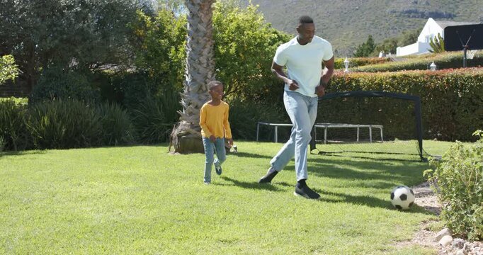 African American father and son on lawn son coming father dribbling son stealing ball playing