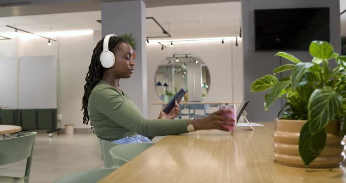 Getting alert, African woman checking phone or tablet for work, sipping cup at coworking, copy space