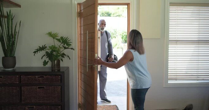 Diverse neighbors shaking hands, woman opening entryway, man in gray scrubs entering with black bag