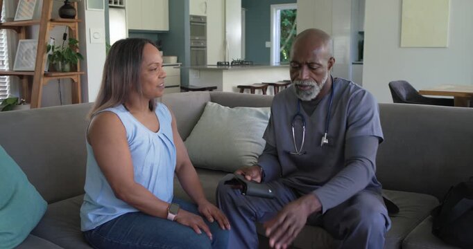 Mature woman gesturing, African American clinician preparing monitor, applying cuff at BP check