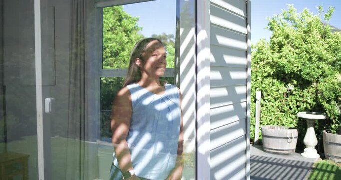 Woman standing inside sliding glass door, camera moving closer, turning toward striped shadows