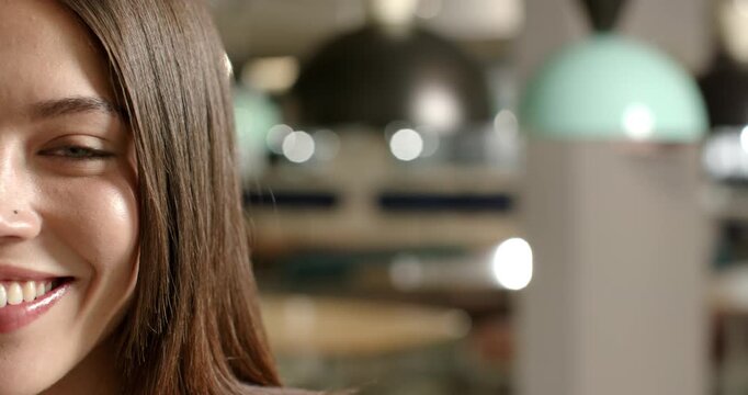 Woman is shifting from smile into laugh reacting to off-frame joke near pendant lamps in cafe