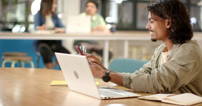 African American man tapping smartphone, placing phone, and typing on laptop at coworking table