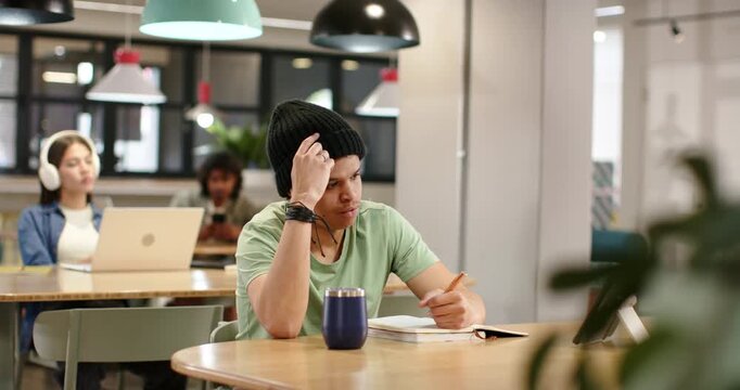 African American man in hat pausing tapping pencil writing notebook and sorting ideas at workspace