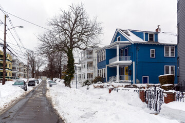 Blue suburban house along snowy residential street in Brighton Massachusetts Greater Boston winter landscape
