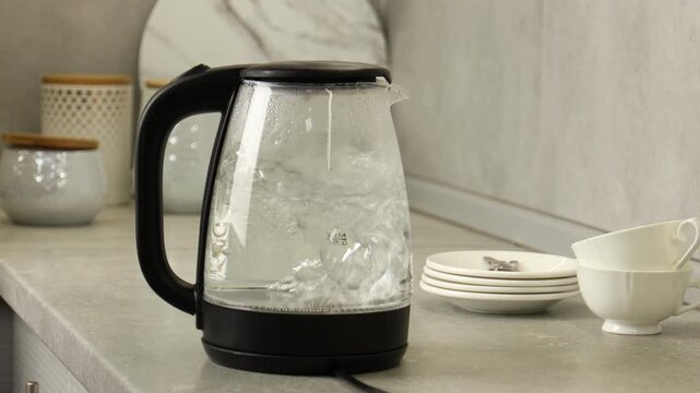 Water boiling in electric kettle and woman taking cup to make tea in kitchen, closeup