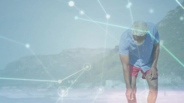 Vertical video: Senior man walking on beach spotting small item and crouching as tech nodes glow