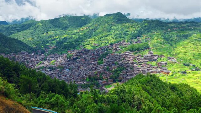 Panoramic view of Xijiang Qianhu Miao Village featuring traditional wooden houses and lush green terraced rice fields in Guizhou, China.