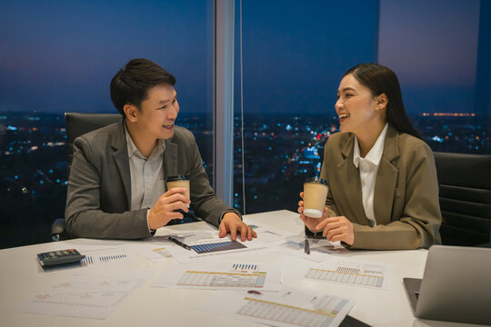 two happy business colleagues meeting and having a casual conversation and drinking coffee in office at night