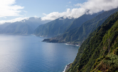 Obraz premium Seixal village on Madeira Island's northwest coast. Lush green cliffs meet the Atlantic Ocean's deep blue waters. Scenic view of mountainous terrain under a partly cloudy sky.