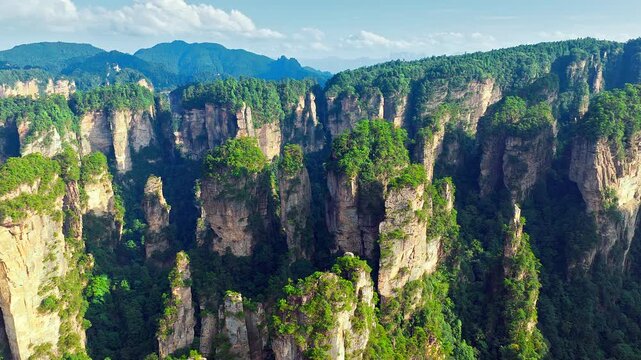 Scenic aerial view of unique quartz-sandstone pillars in Zhangjiajie, Hunan, China, featuring lush green vegetation and breathtaking mountain landscape under blue sky.