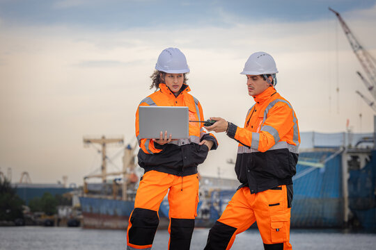Engineers with laptop and radio coordinating cargo ship operations at port, Professional technical team in safety uniform monitoring international shipping logistics