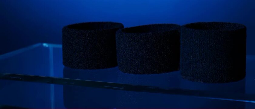 Woven Wristband Pair. Soccer/Football Merchandise Mockup (No Brand, No Logo). Product Mockup. two matching unbranded black wristbands made of thick absorbent cotton, set on a simple glass surface
