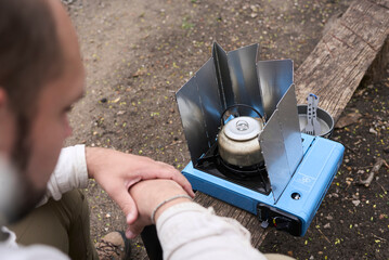 Hispanic man uses a windbreaker to be able to heat water on his camping gas stove even if it is windy. © Carolina Jaramillo