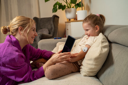 Mother checking her cute little daughter CGM sensor to see blood sugar level in app via smartphone