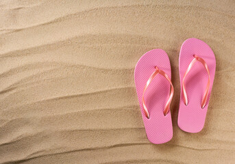 Fototapeta premium pink female flip flops on a beach sand, top view.