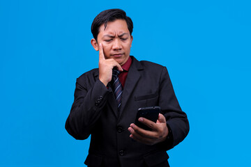 Businessman In Thoughtful Checking Phone Isolated On Blue Background