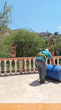 Worker rolling and positioning a blue plastic drum outdoors