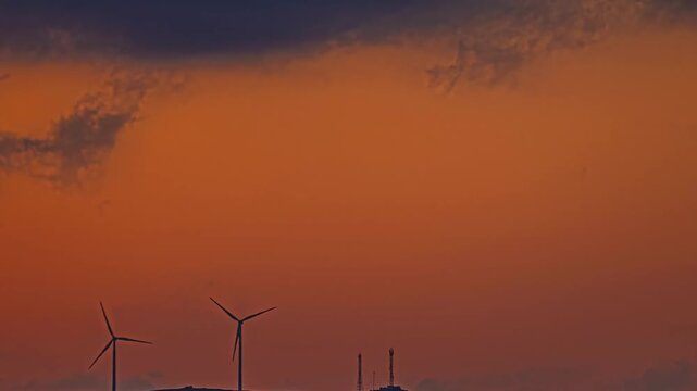 Time lapse of wind turbines spinning under dramatic orange sunset sky