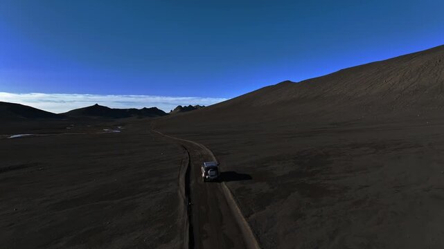 Drone follow shot of a 4x4 driving a lonely dirt road through Iceland&rsquo;s black volcanic desert under deep blue sky. Epic remote travel, solitude, and off-grid adventure.