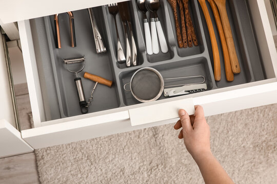 Woman opening drawer of utensils in kitchen, top view
