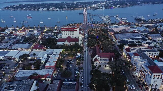 Historic city street in St. Augustine, Florida, overlooking a waterfront marina with boats, illuminated streets, and buildings at dusk with a calm and scenic atmosphere.