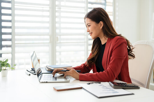 Asian business woman using laptop computer typing And working online sitting at desk in office wearing suit. Office worker lady browsing internet on computer. Entrepreneurship.