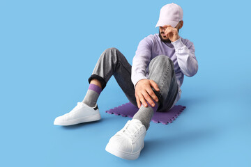 Man in cap with stylish sneakers sitting on blue background