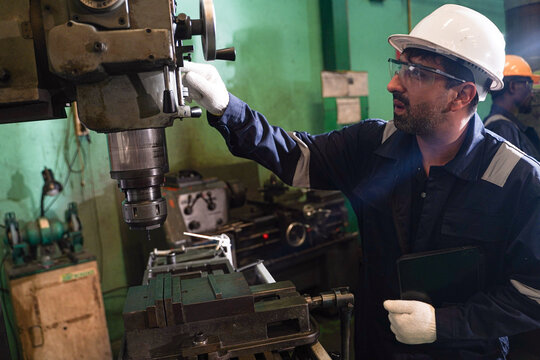 Multi-ethnic team of professional engineers and technicians operating heavy machinery and using digital tablets for production control in a modern factory.