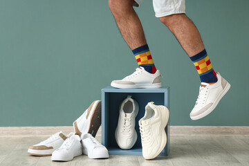 Naklejka premium Male legs with stylish sneakers and shelf near green wall