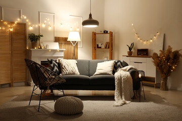 Naklejka premium Interior of living room with sofa, armchair and glowing lights in evening