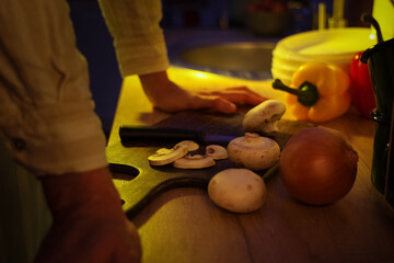 Young man with mushrooms on cutting board in kitchen at night, closeup