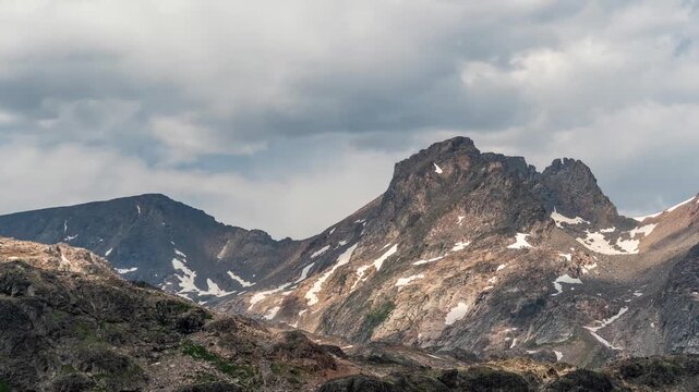 Clouds and patches of sunlight moving over a jagged rocky peak with snow patches, Beartooth Mountains, Montana, time lapse