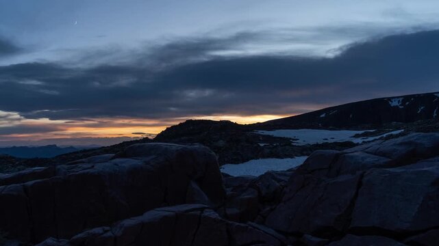 Golden sunset glowing under dark clouds behind granite boulders, fading to dusk, Beartooth Plateau, Montana, time lapse