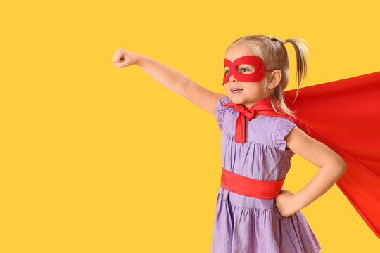 Cute little girl dressed as superhero on orange background