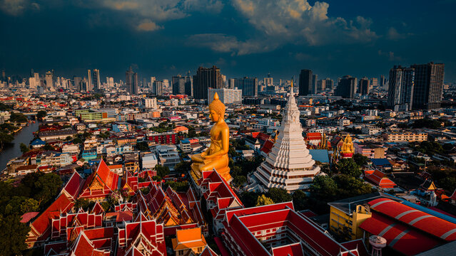 Spectacular aerial view of the giant golden Buddha statue and stupa at Wat Paknam Bhasicharoen with dramatic sky and sunbeams in Bangkok, Thailand.