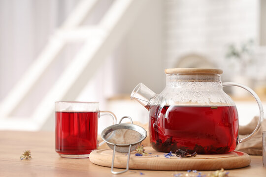 Teapot and cup with healthy hibiscus tea on table in kitchen