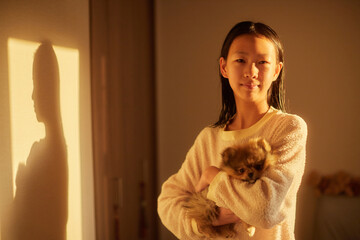 家の寝室で朝の日差しを浴びて子犬を抱っこする可愛い女子中学生の姿