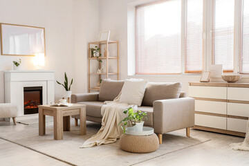 Naklejka premium Interior of light living room with grey sofa, coffee table and fireplace