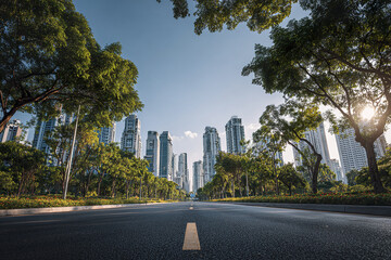 Obraz premium Modern city skyline with tall buildings and green trees lining empty road under clear blue sky during sunny day