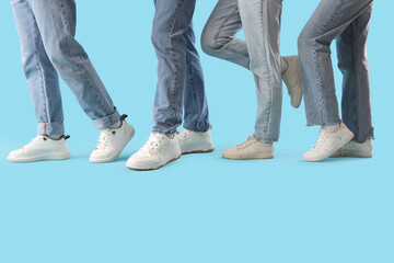 Legs of people in jeans with white sneakers on blue background