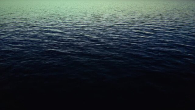 Smooth ocean surface with gentle ripples reflects warm sunset colors under a clear sky, creating a serene and peaceful marine atmosphere in unidentifiable location.